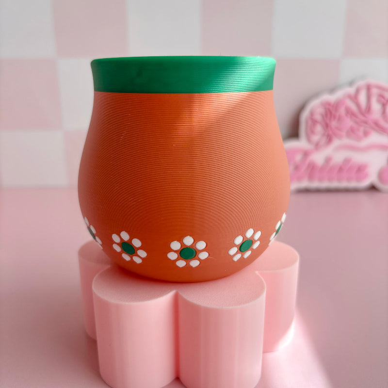 3d Printed terracotta pots with green rims on a pink surface with decorative items.