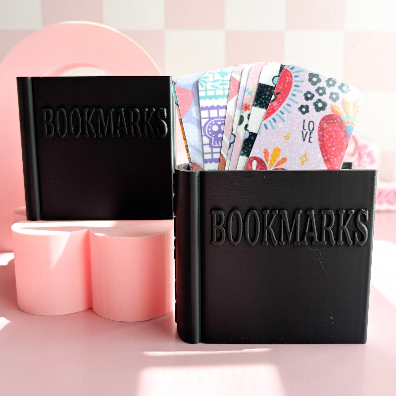 Black 'BOOKMARKS' holder with colorful bookmarks on a pink background