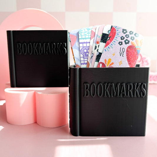 Black 'BOOKMARKS' holder with colorful bookmarks on a pink background