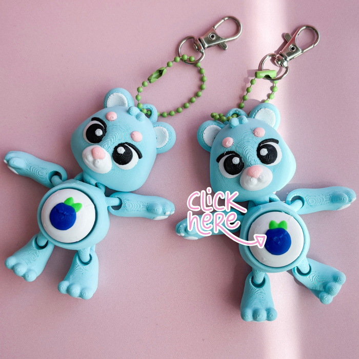 Two blue cartoon character keychains on a pink background with 'Click here' text overlay.
