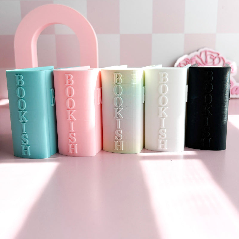 Five book-shaped tumblers with 'BOOKISH' text on a pink surface.