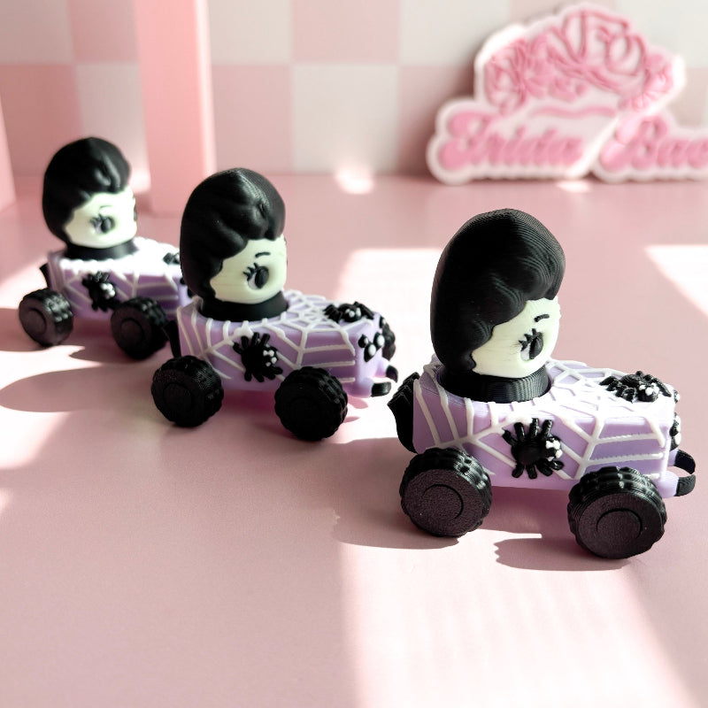 Three small toy cars with figurine fidget clicker with skeleton characters on a pink checkered background