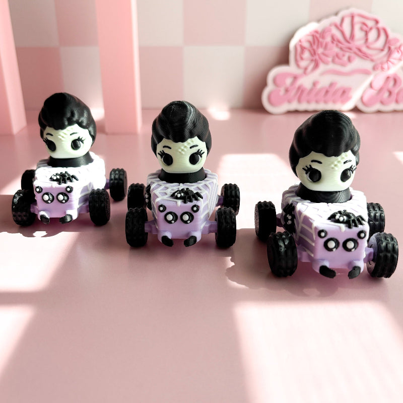 Three small toy cars with figurine fidget clicker with skeleton characters on a pink checkered background