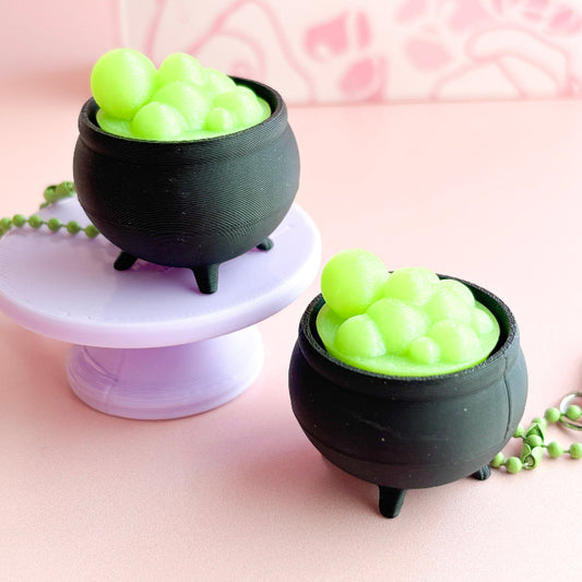 Two black cauldron-shaped containers with green contents on a pink background