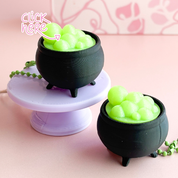 Two black cauldron-shaped containers with green contents on a pink background