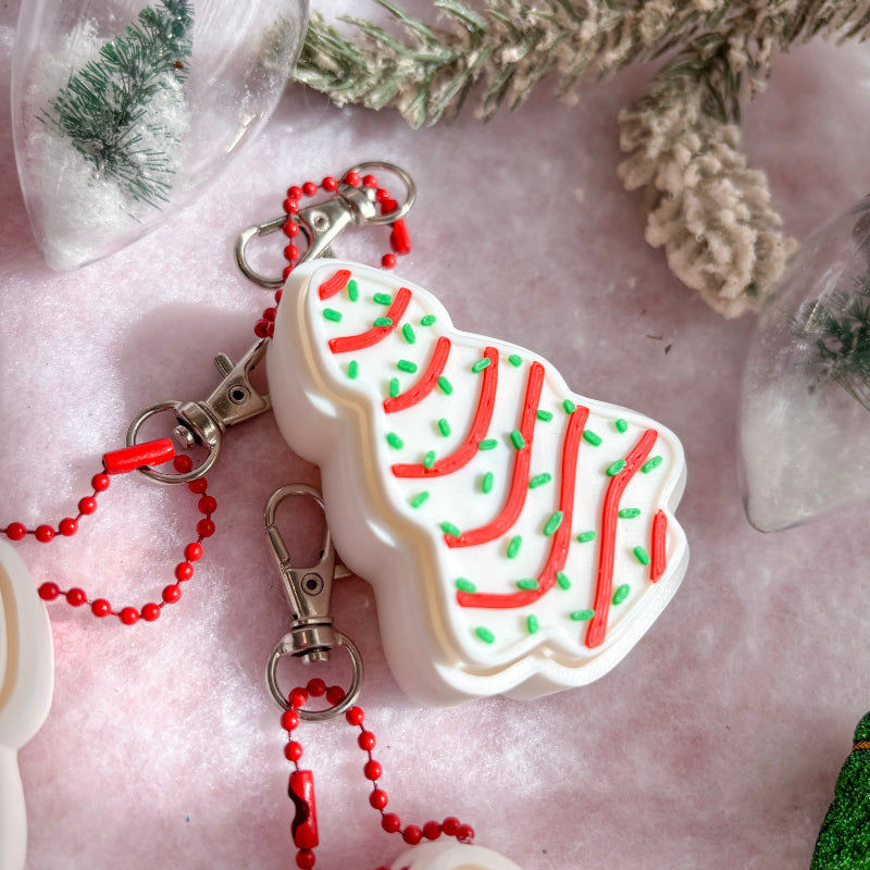 Christmas-themed keychain with red and green decorations on a pink surface.