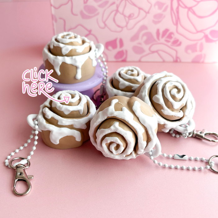 Cinnamon roll shaped keychains with white icing on a pink background