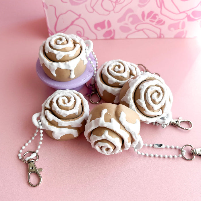 Cinnabon-shaped keychains with white icing on a pink background