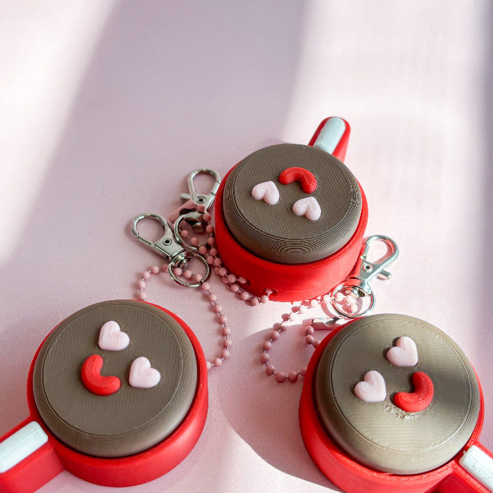 Three red and gray keychains with smiley face designs on a light pink background