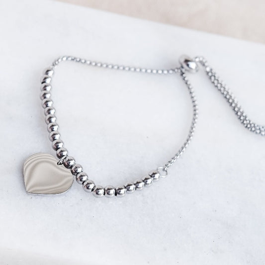 Experience the perfect blend of style and sentiment with our RAYNE CORAZON BEADED BRACELET in SILVER! Crafted from durable stainless steel, this adjustable bracelet features an engravable heart pendant charm, making it the ideal personalized accessory for any special occasion. The adjustable chain ensures a comfortable fit for all wrist sizes.