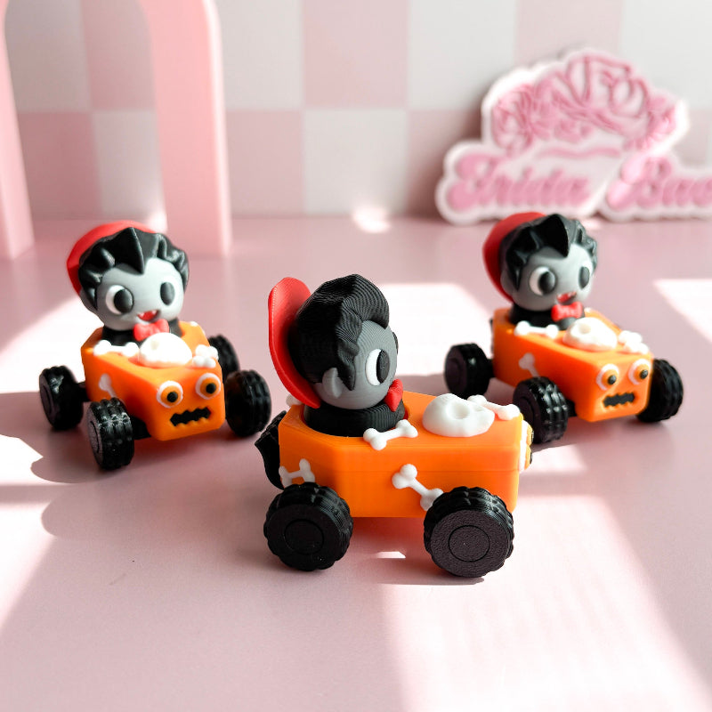 Three small toy cars with figurine fidget clicker with skeleton characters on a pink checkered background