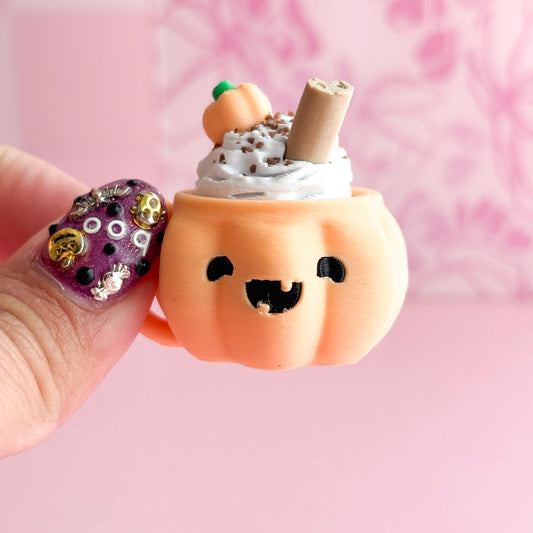 Pumpkin-shaped ice cream with whipped cream and a straw, held by a hand against a pink background.