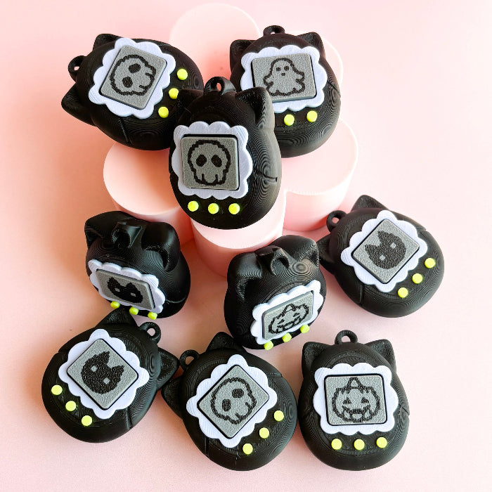 Black cat-shaped charms with skull designs on a pink background