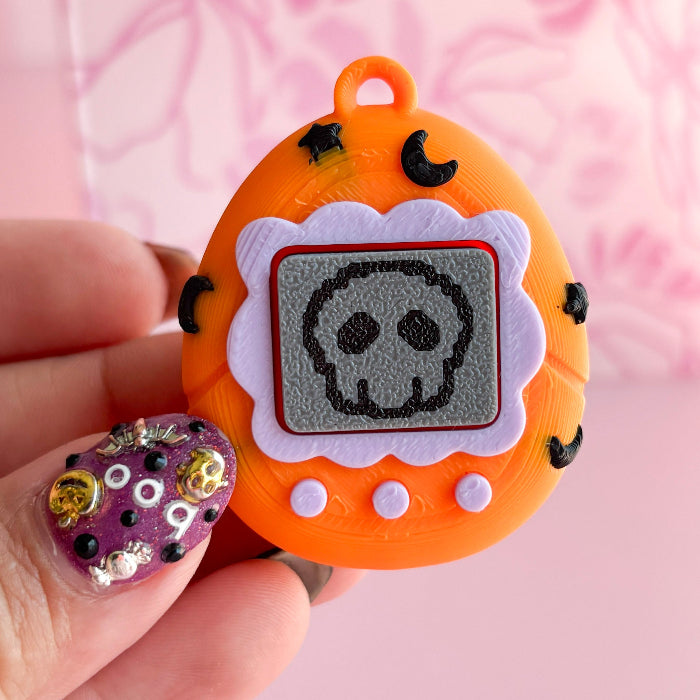 Orange toy with skull design held by a hand against a pink background