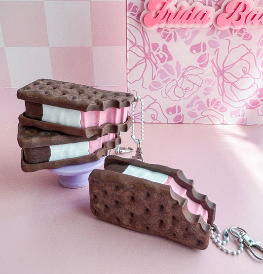 Chocolate cookie sandwich keychain on a pink surface with a decorative background