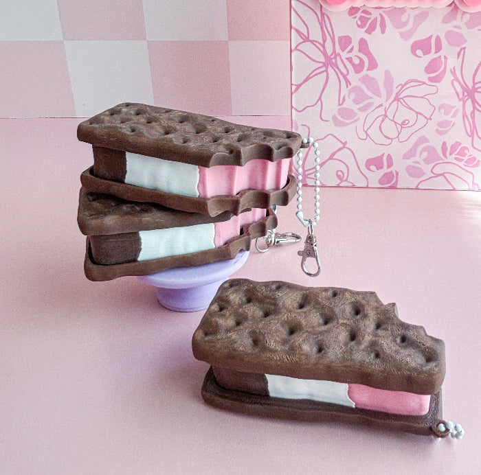 Ice cream sandwich-shaped keychains on a pink surface with a floral-patterned wall in the background.