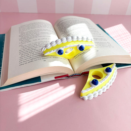Yellow book holder with blueberries in an open book against a pink checkered background