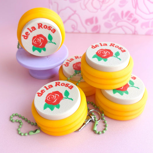 Yellow containers with 'de la Rosa' branding and a rose design on a pink background