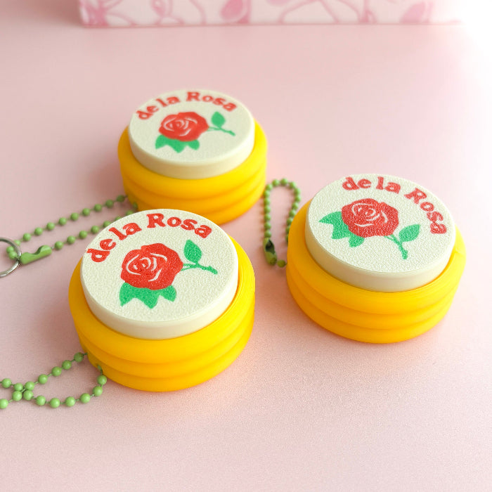 Three yellow containers with 'de la Rosa' branding and a rose logo on a pink background.