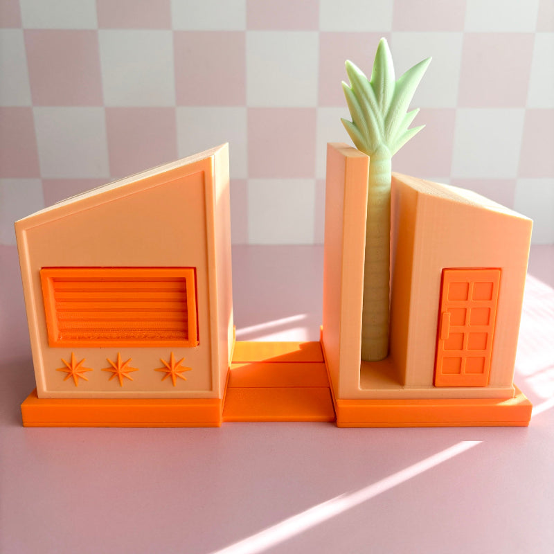 Decorative bookends with a house design and a small potted plant on a checkered background