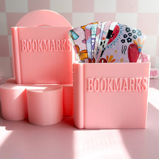 Pink 'BOOKMARKS' holder with colorful bookmarks on a light pink background