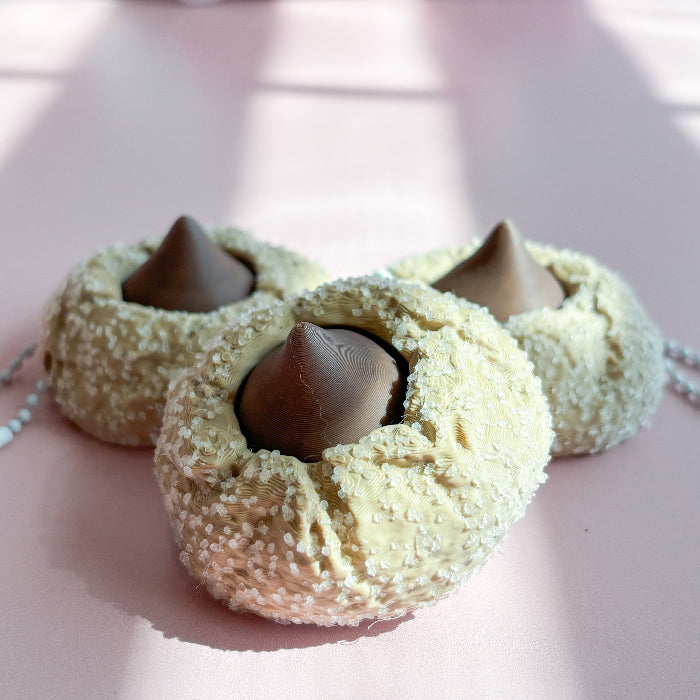 Three cookie-shaped fidget clickers with chocolate centers on a pink background