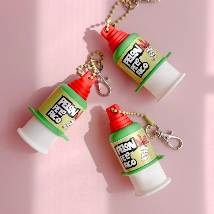 Three colorful plastic containers clickers with red lids and 'Pelon Peló Rico' branding on a pink background.