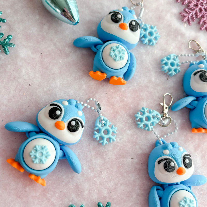 Colorful penguin keychains with snowflake and star decorations on a textured surface.