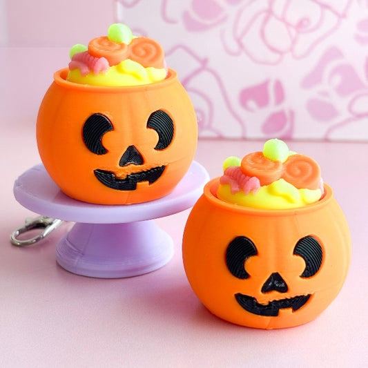 Two Halloween-themed jack-o'-lantern candy containers on a pink stand with a pink background.