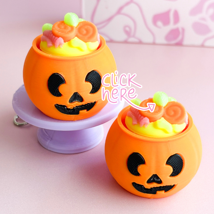 Two Halloween-themed orange containers with candy on a pink background