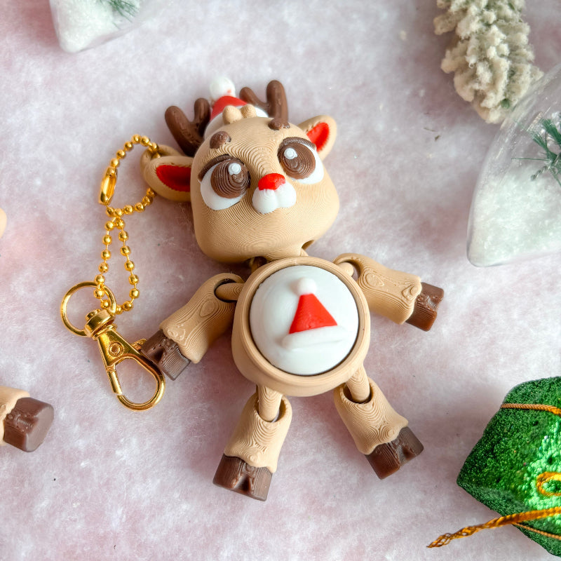 Toy reindeer with a gold keychain on a light pink surface with decorative elements.