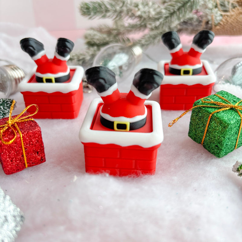 Christmas-themed figurines of Santa stuck in chimney with presents and a tree in the background.