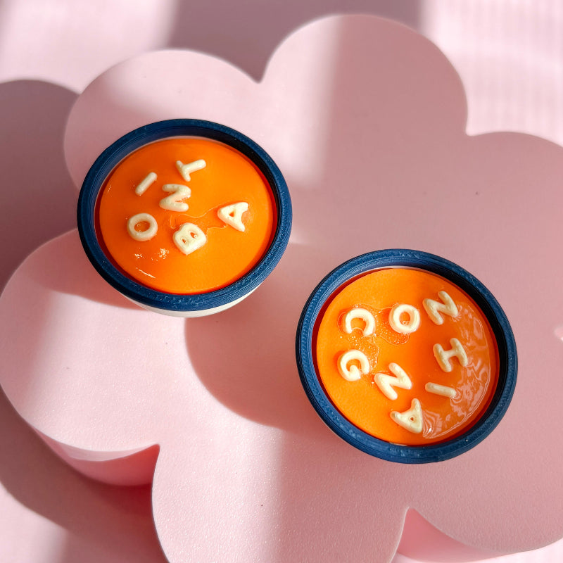 Two orange soup clickers containers with blue rims on a pink flower-shaped stand.