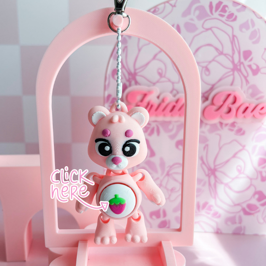 Pink teddy bear keychain with a strawberry design on a pink stand.