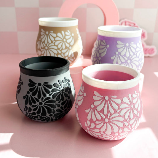 Set of four decorative cups with floral patterns on a pink surface.