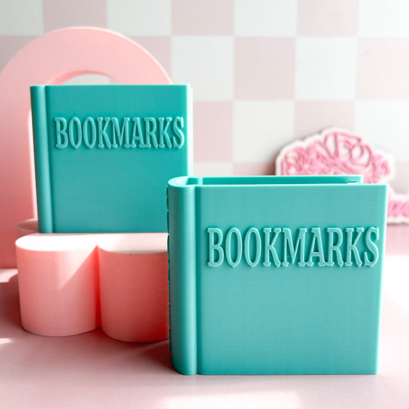 Two turquoise book-shaped containers with 'BOOKMARKS' text on a pink and white checkered background.
