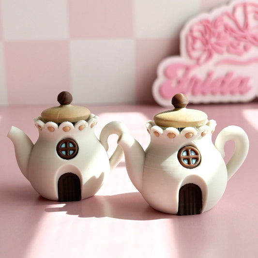 Two 3D printed teapot clickers shaped like small houses on a pink surface with a blurred background.