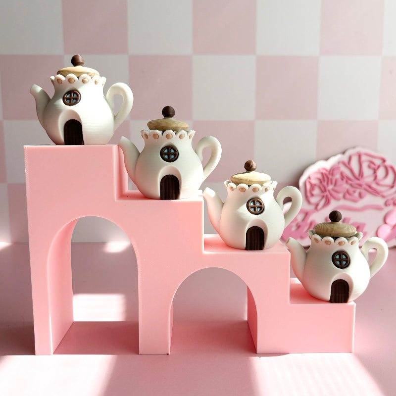 3D printed teapot clickers shaped like small houses on a pink surface with a blurred background.