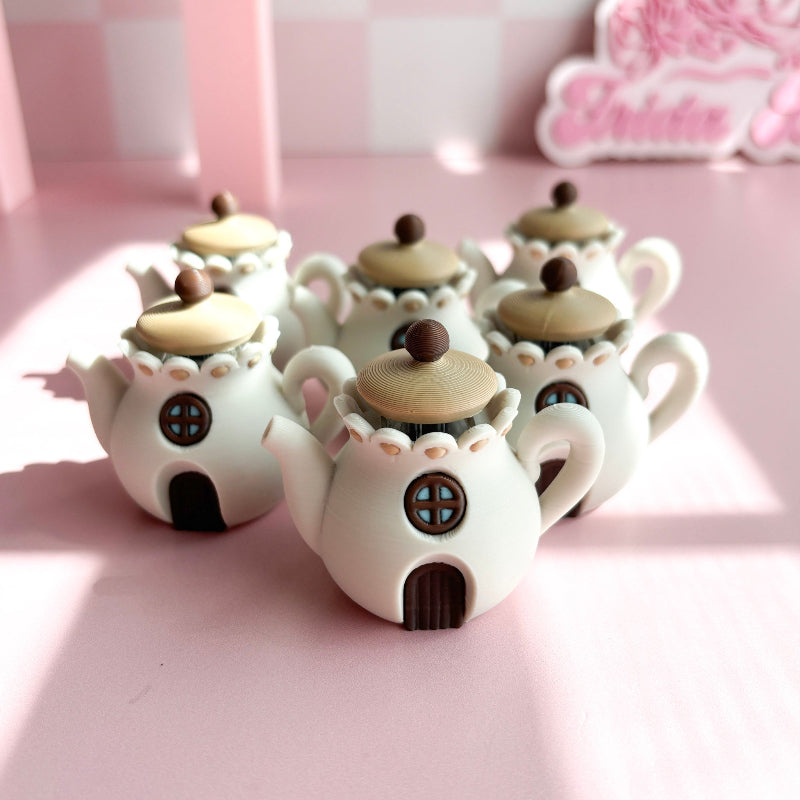 3D printed teapot clickers shaped like small houses on a pink surface with a blurred background.