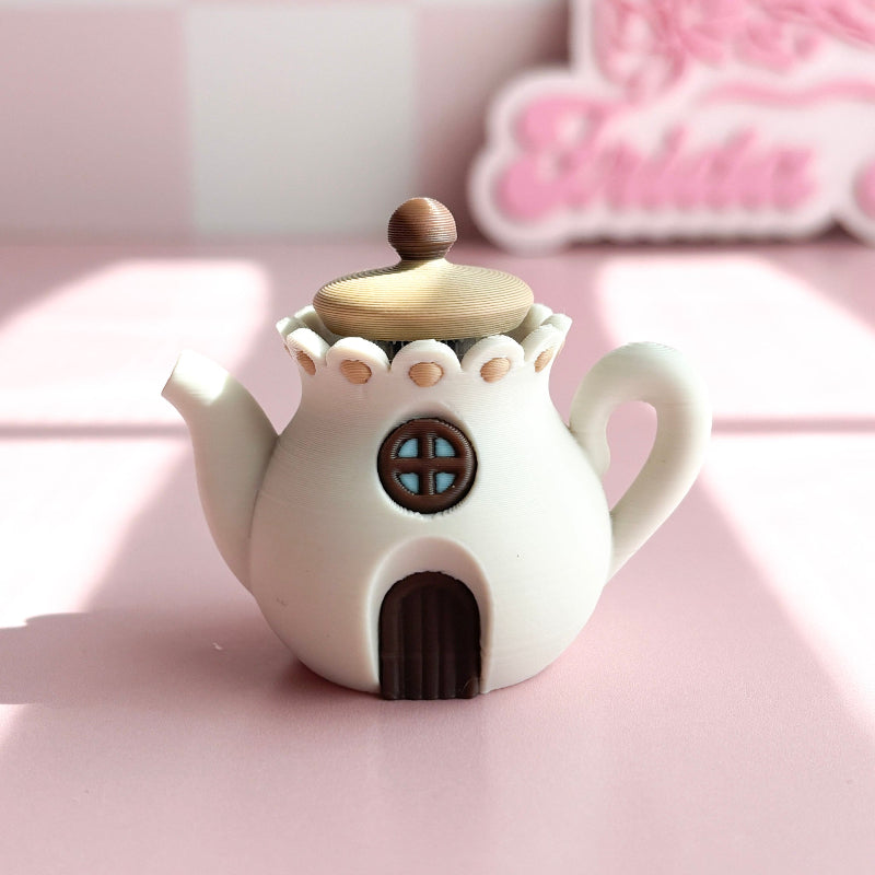 3D printed teapot clickers shaped like small houses on a pink surface with a blurred background.