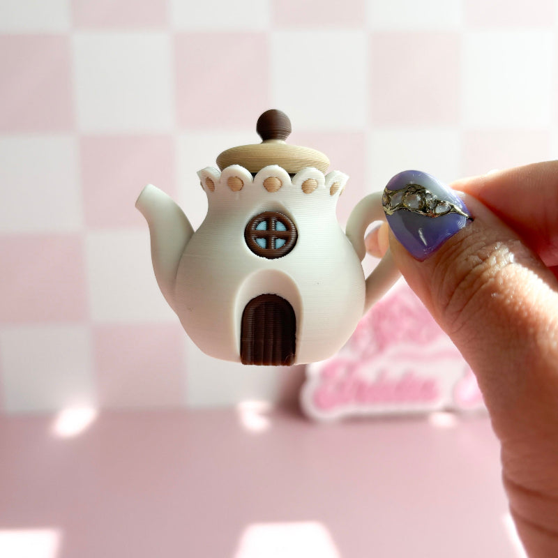 3D printed teapot clickers shaped like small houses on a pink surface with a blurred background.