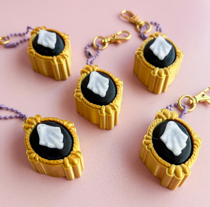Gold and black keychains with a white stone on a pink background