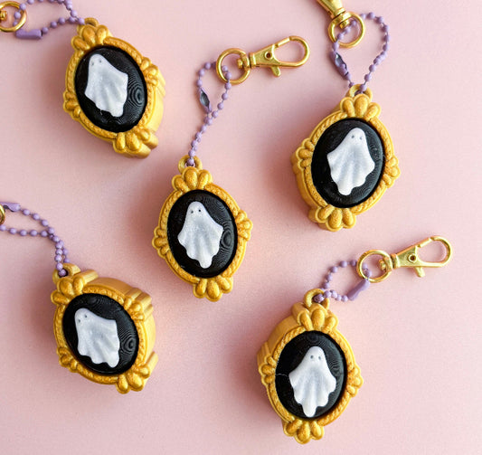 Gold-framed keychains with ghost designs on a pink background