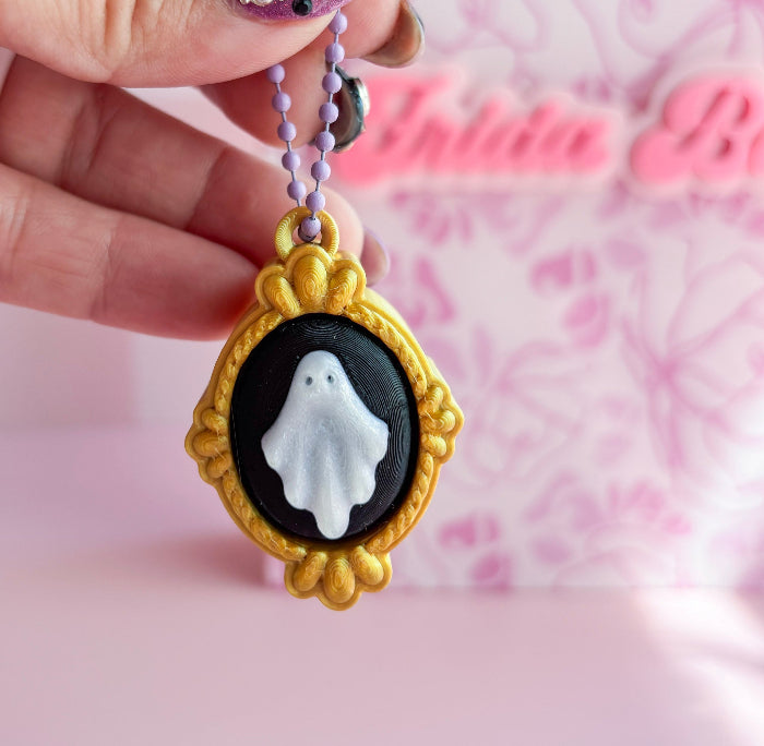 Ghost pendant  held by a hand against a pink background