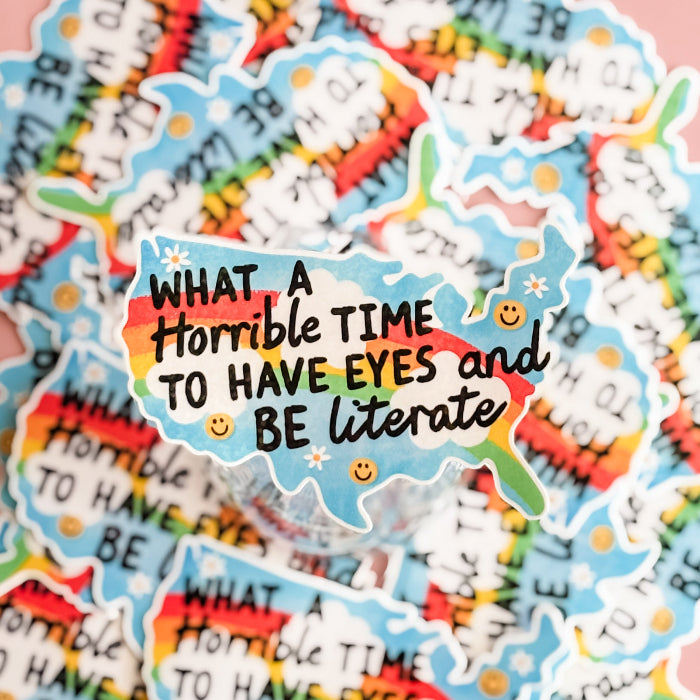 Colorful sticker with text 'What a horrible time to have eyes and be literate' on a multicolored background.