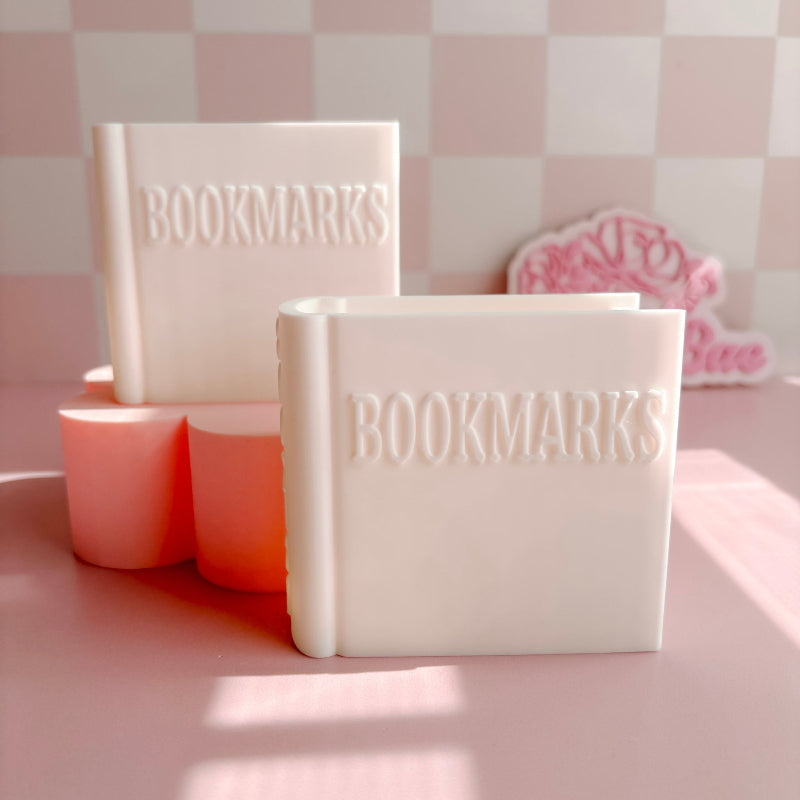 Two white books labeled 'BOOKMARKS' on a pink surface with a checkered wall background.