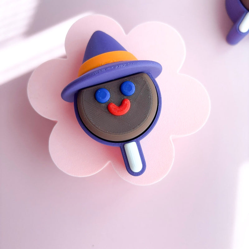 Five Halloween-themed lollipop shaped figurines with purple hats on a pink background