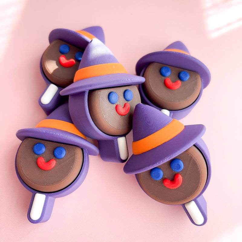 Five Halloween-themed lollipop shaped figurines with purple hats on a pink background