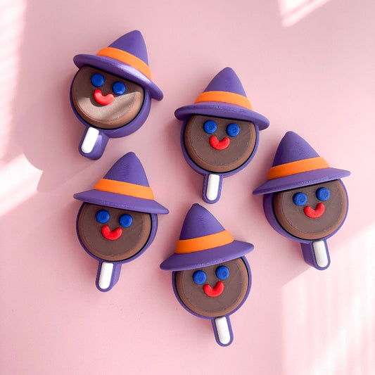 Five Halloween-themed lollipop shaped figurines with purple hats on a pink background