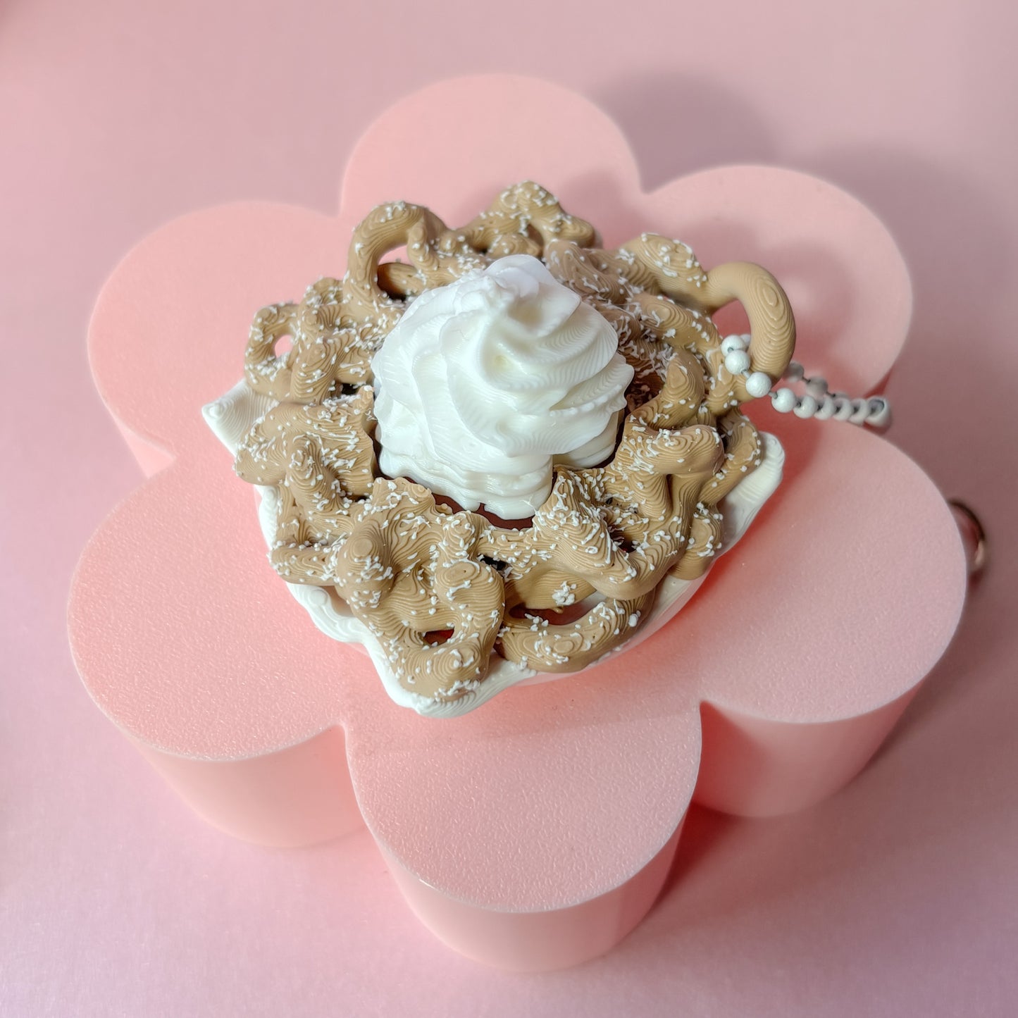 Keychains shaped like funnel cake with white frosting on a pink checkered background